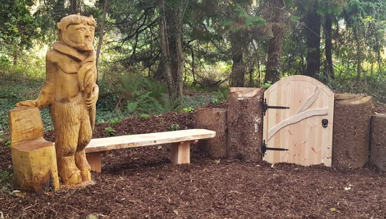 Mr Tumnus wooden sculpture beside a bench and wardrobe gate on the Narnia Trail